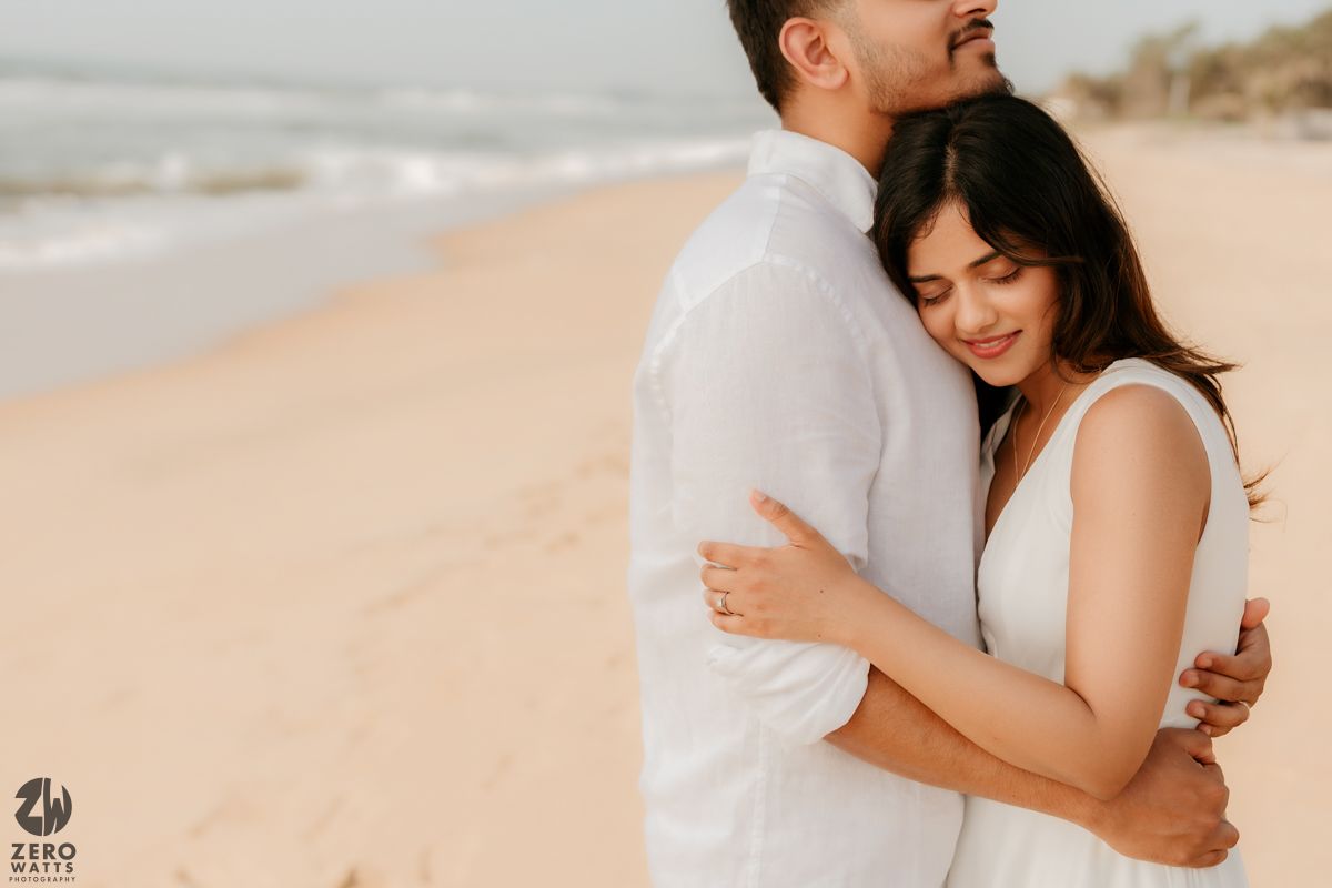 Two people in romantic embrace at a sun-drenched beach with golden sand and soft lighting.