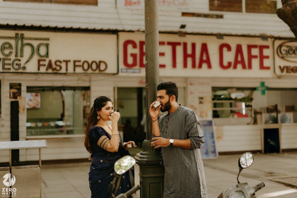 A couple shares an intimate moment with takeout drinks while sitting on steps outside a cafe storefront.