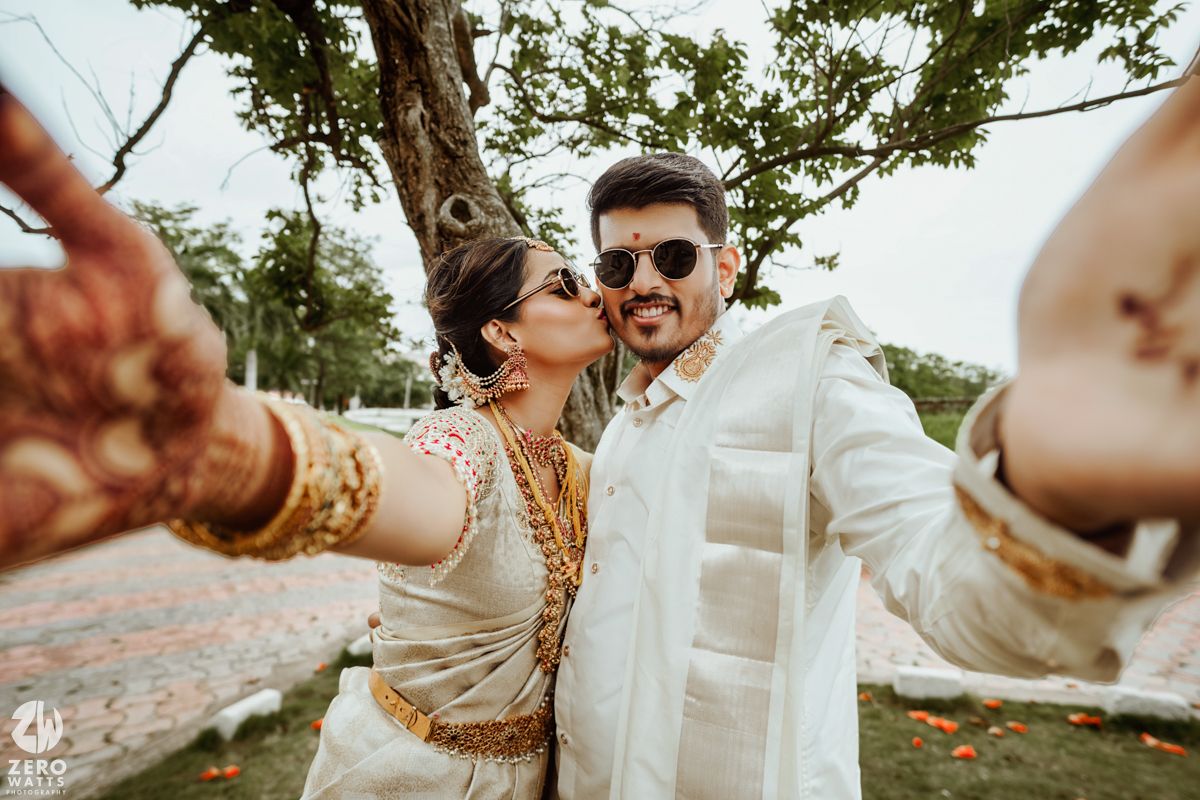 A couple shares joyful moments during their outdoor wedding photoshoot under sunlit trees.