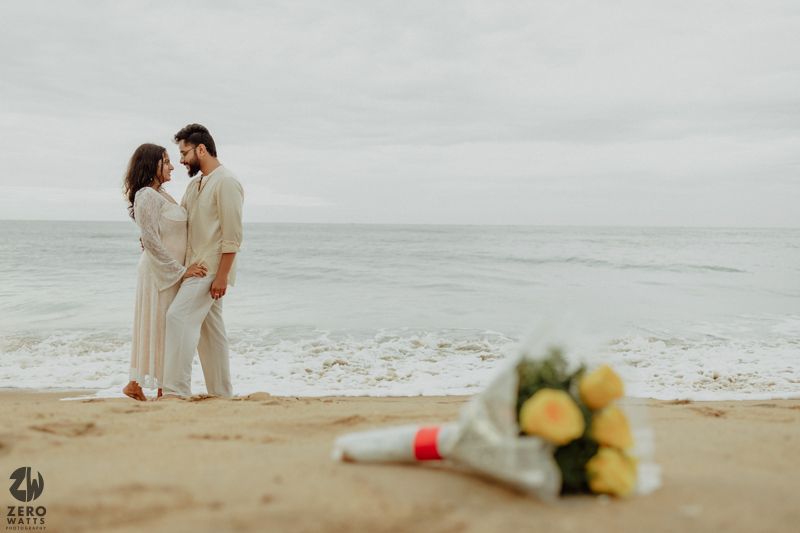 Romantic beach photoshoot with gentle waves and overcast sky.