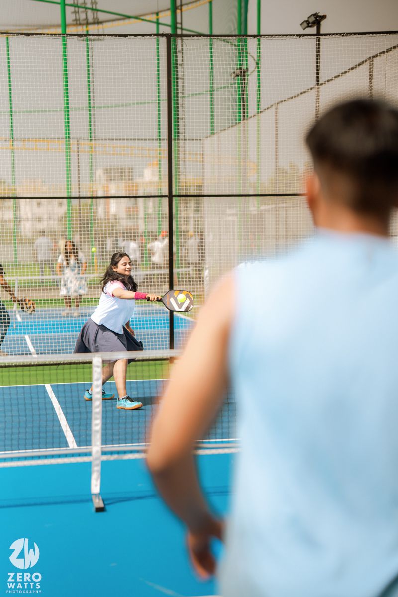 Pickleball players engaged in a match on an outdoor blue court with protective netting.