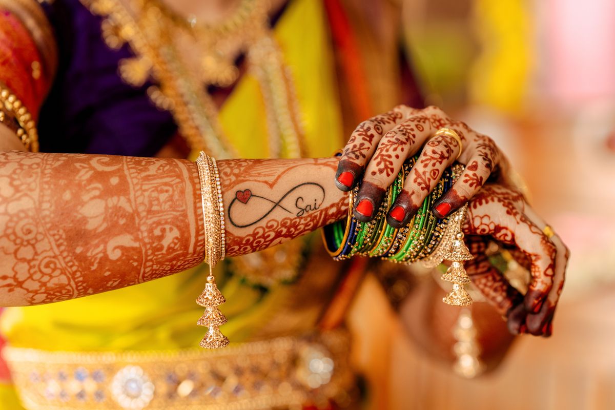 Intricate mehndi design on hands adorned with bangles and rings at an Indian wedding ceremony.