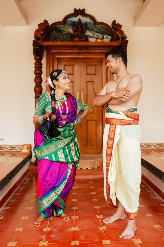Traditional South Indian classical dancers in traditional attire performing at an ornate doorway with red floor tiles.