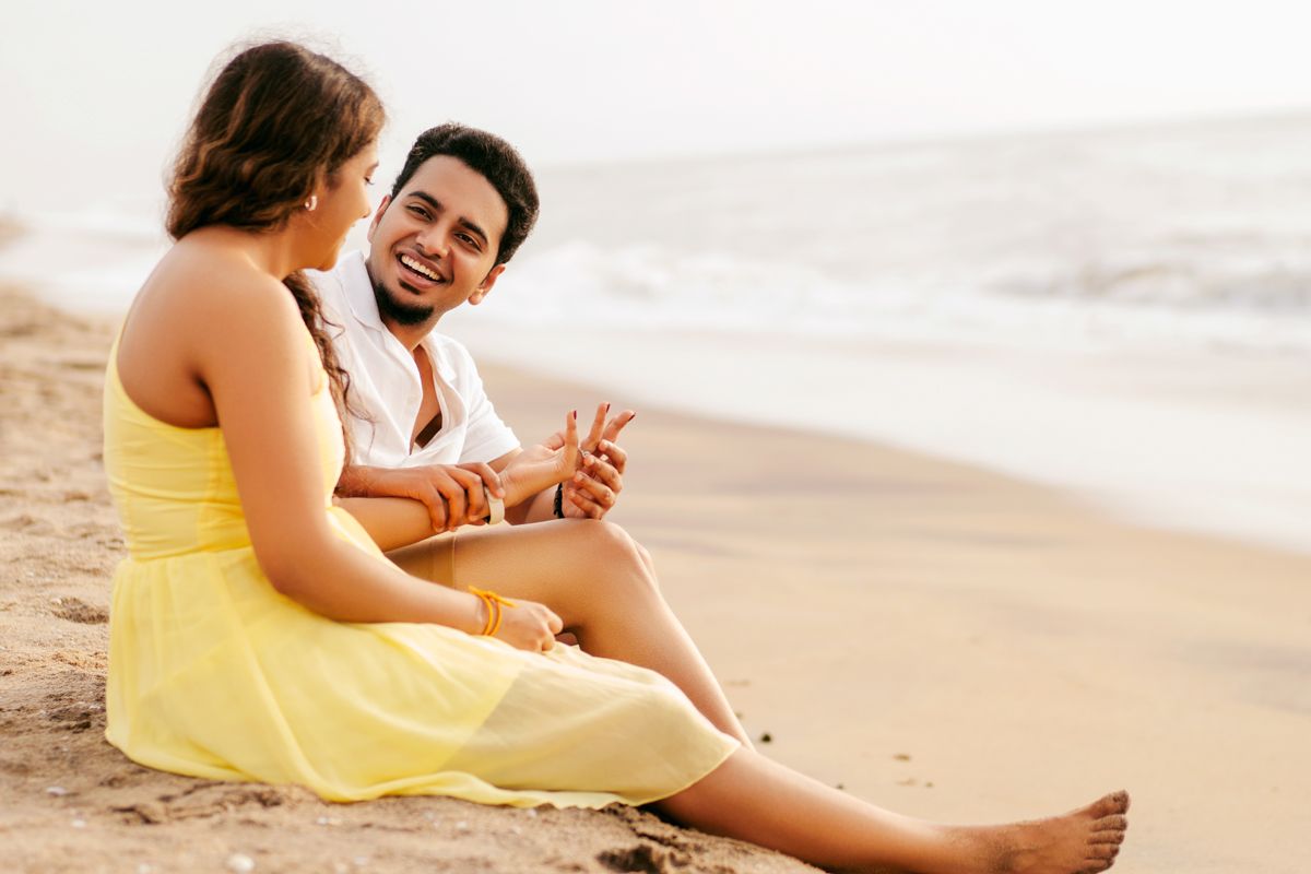 A couple sits on a sandy beach, sharing a joyful conversation in the warm sunlight.