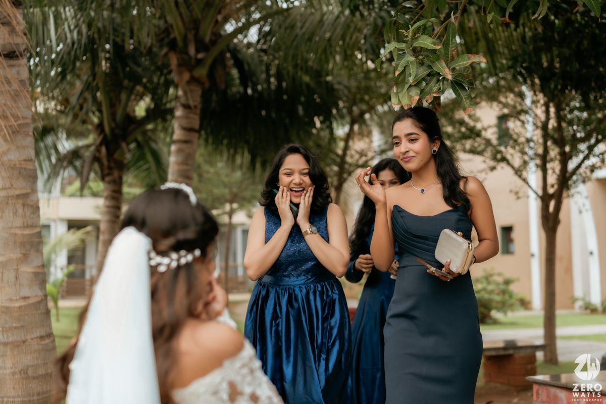Bridesmaids in navy and dark dresses react with excitement to the bride during a wedding photoshoot.