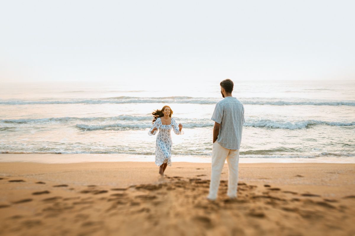 Parent and child holding hands while walking along ocean shoreline at sunset.