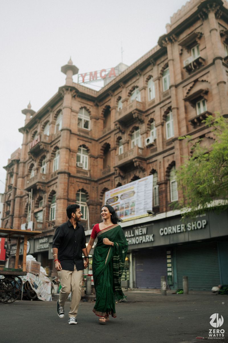 A couple walking past a historic colonial building with ornate architecture in an urban setting.
