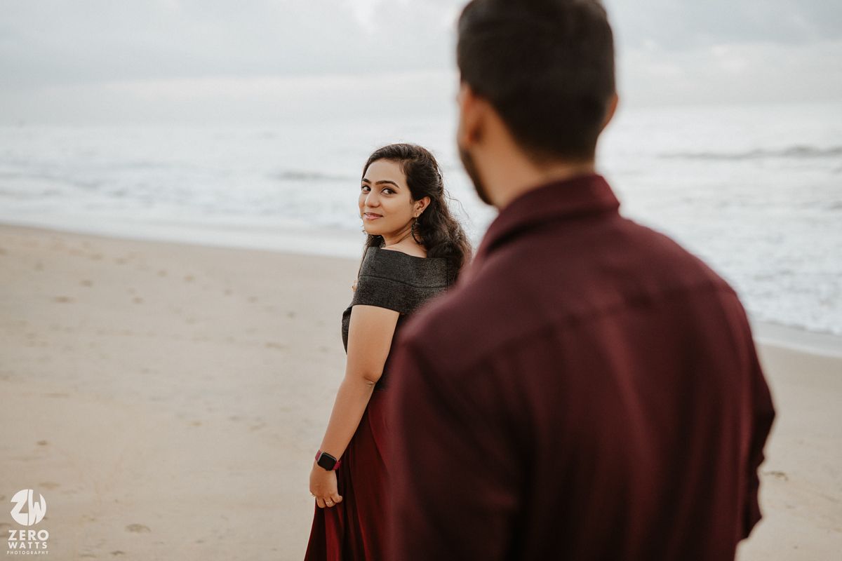 A couple on a moody beach with cloudy skies in maroon and black outfits.