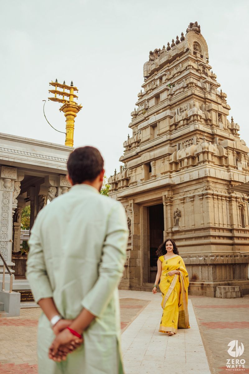A couple poses in traditional Indian attire in front of an ornate temple structure with intricate architecture.
