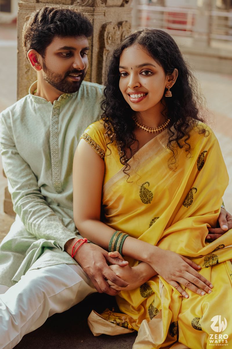 A couple in traditional Indian attire share an intimate moment while sitting together outdoors.