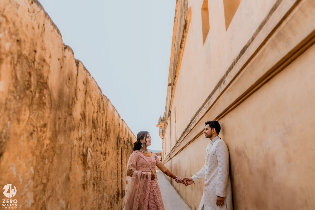 A couple holds hands while walking in a narrow alleyway with peach-colored walls in Rajasthan, India.