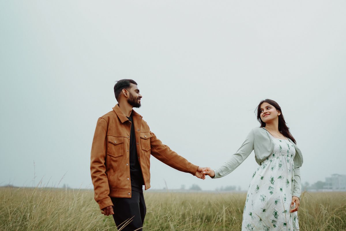 Two people hold hands while standing in a grassy field on an overcast day.