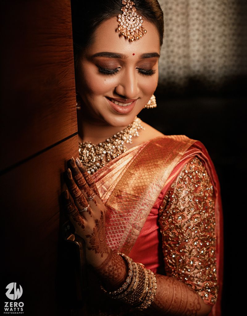 Traditional Indian bride wearing ornate gold jewelry and red silk saree with embroidered sequin details in elegant portrait.