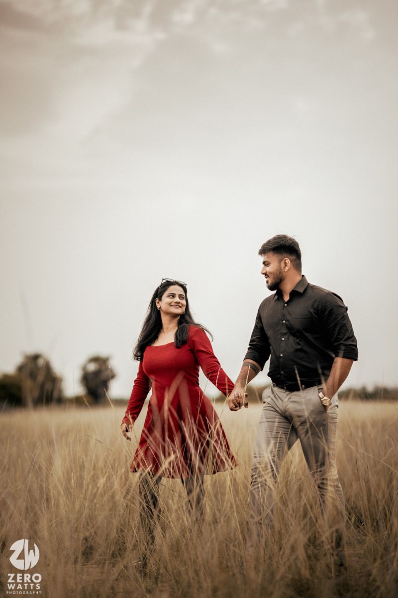 A romantic couple walks hand in hand through a golden wheat field at sunset.