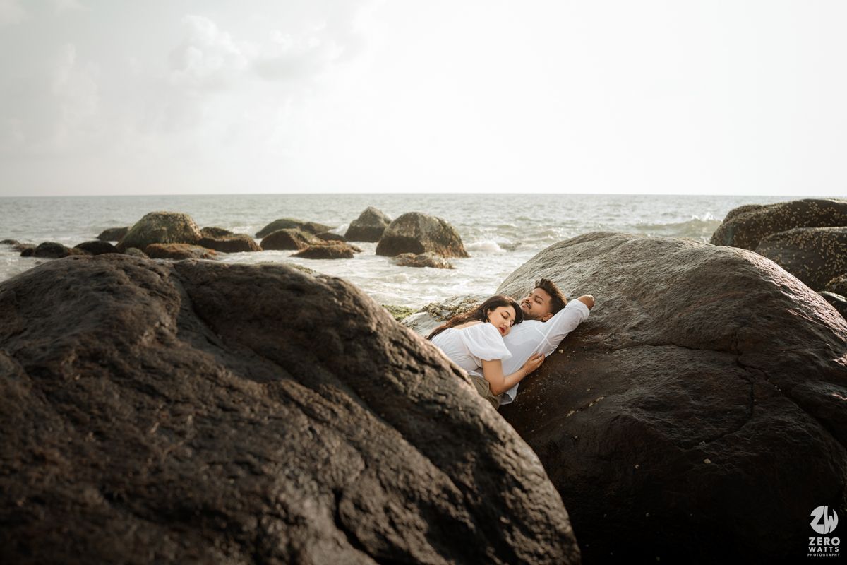 Person lying on dramatic black coastal rocks with ocean waves in background.