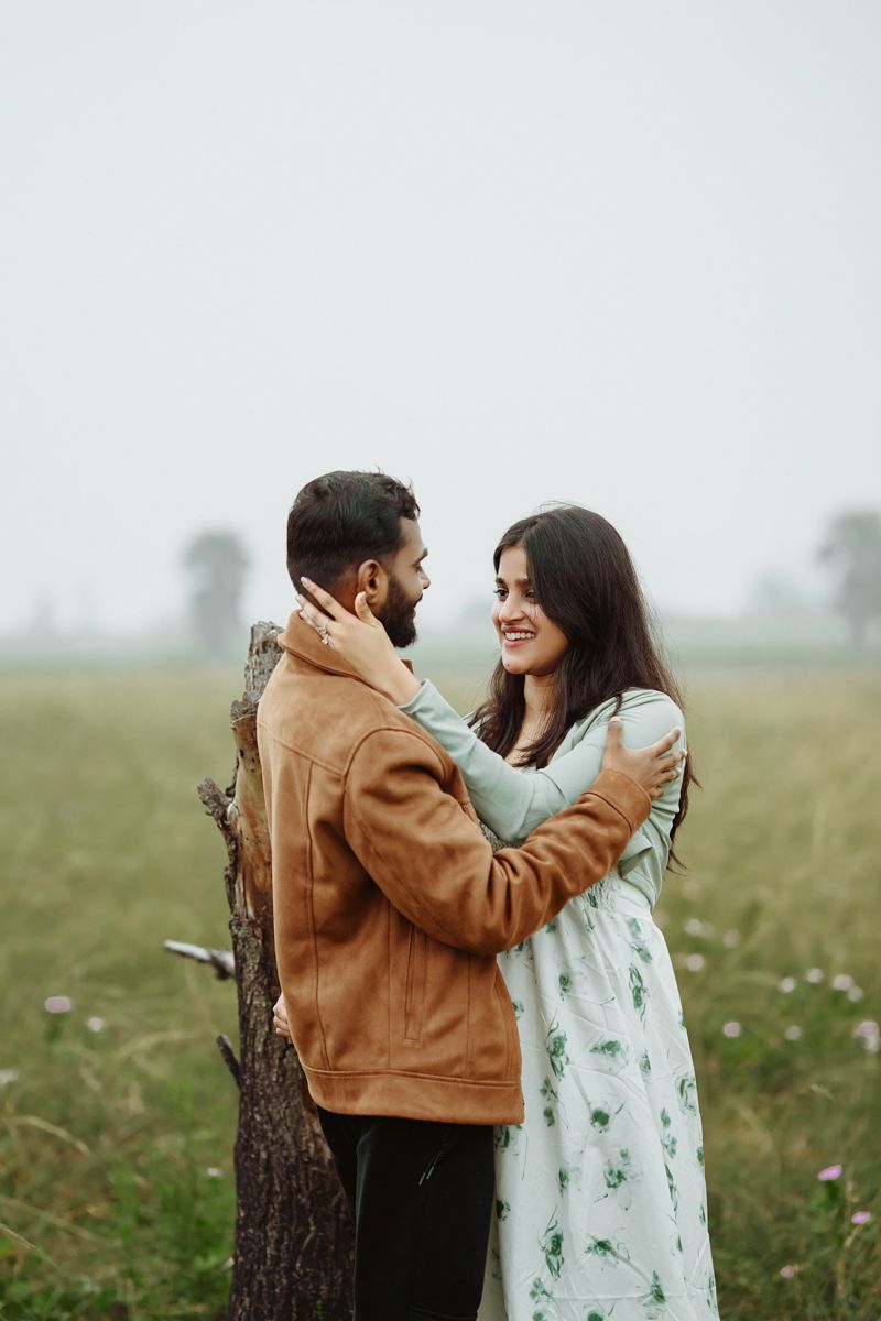 A romantic moment shared between a couple standing by a tree trunk in a field of wildflowers.