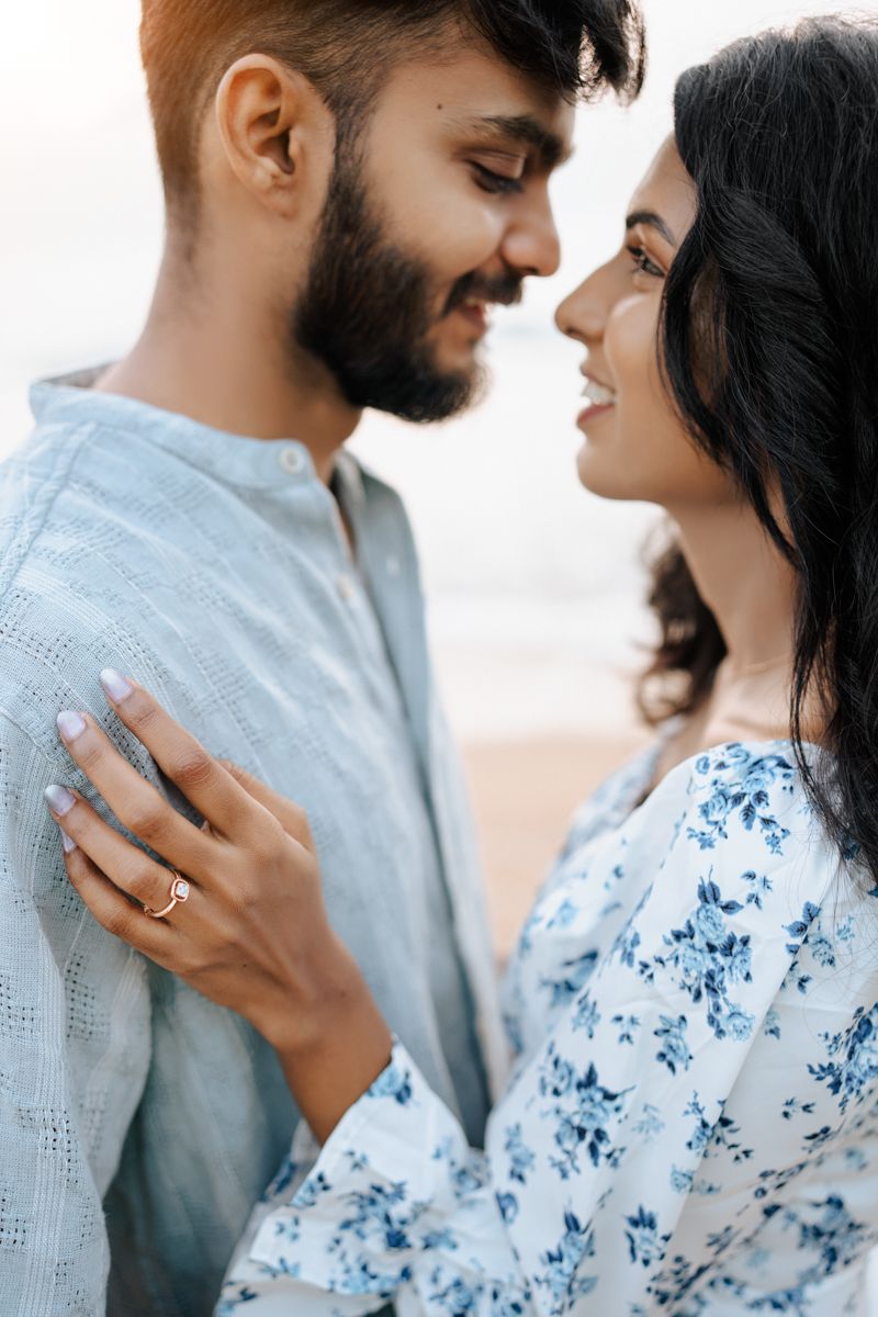 A romantic couple in matching light blue outfits share an intimate moment while showing off an engagement ring.