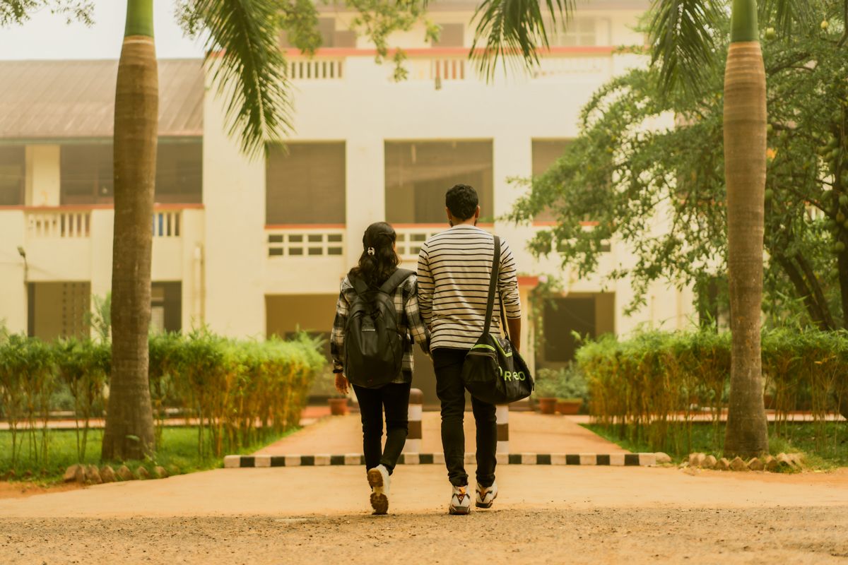 A couple walks together on a palm tree-lined path at a college campus.
