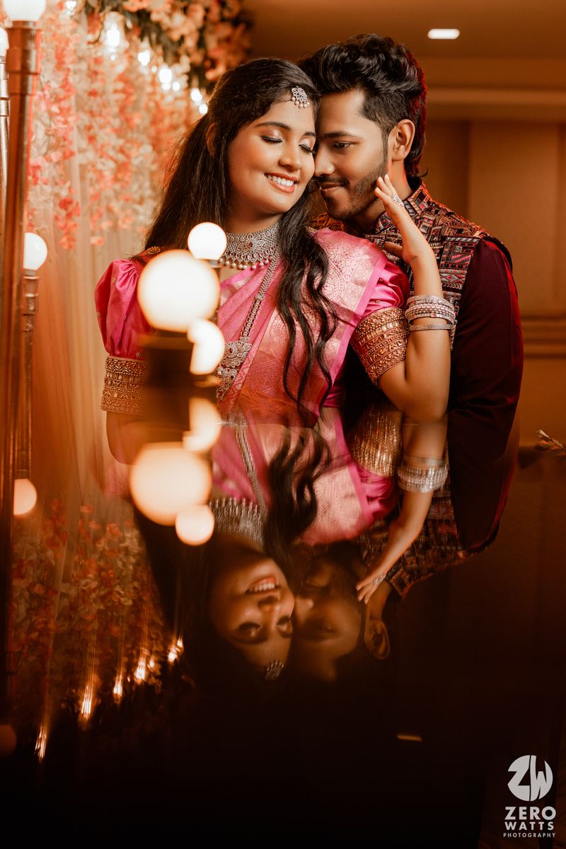 A romantic moment captured with soft bokeh lighting against a decorated indoor venue with hanging floral decor.