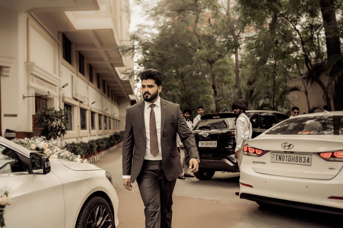 Professional in a dark suit walks past parked cars on a tree-lined street in sepia tones.