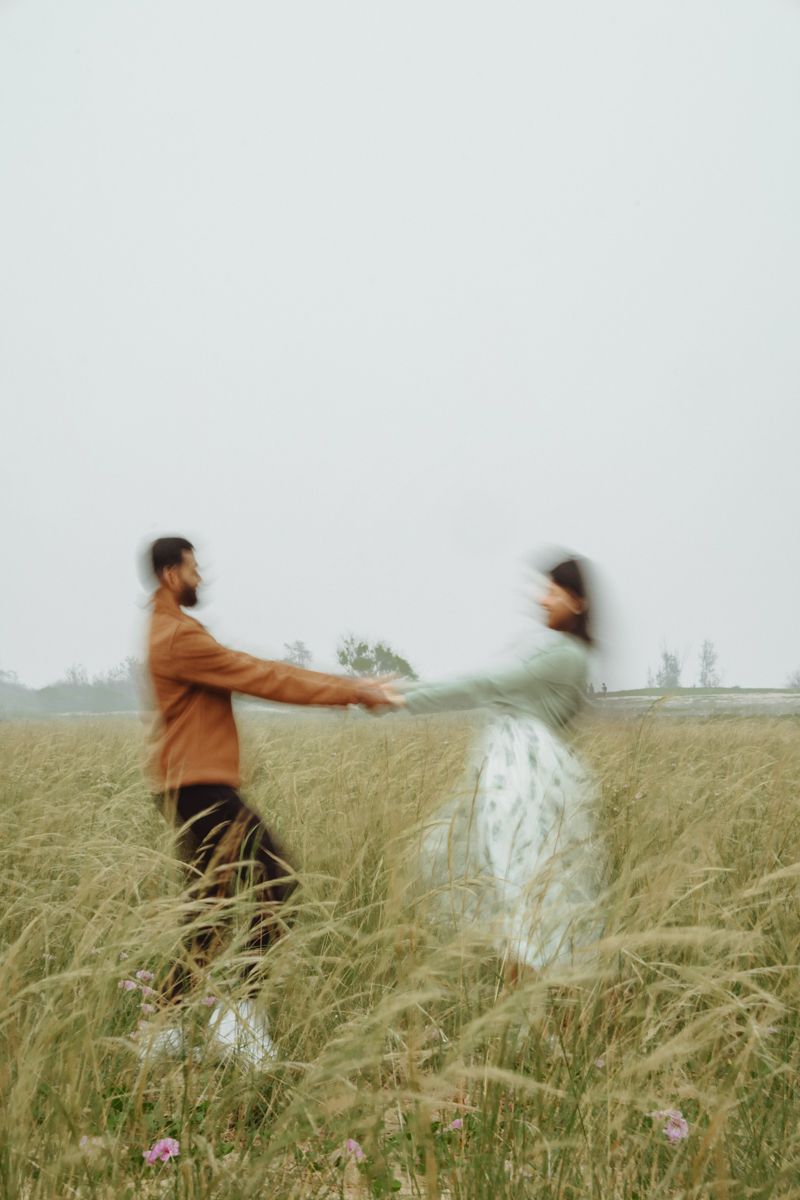 A couple spins joyfully together in a meadow of tall grass on an overcast day.