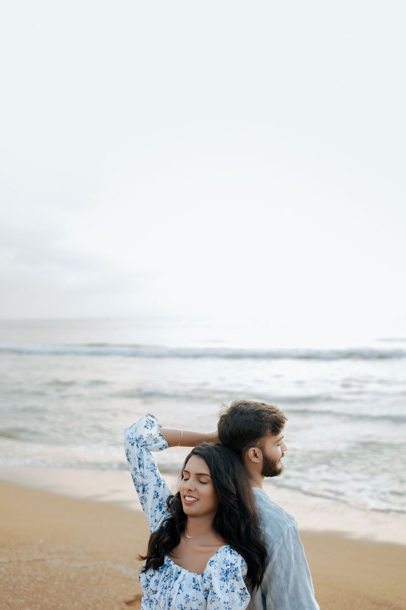 Couple in coordinated blue and grey outfits sharing intimate moment on beach.