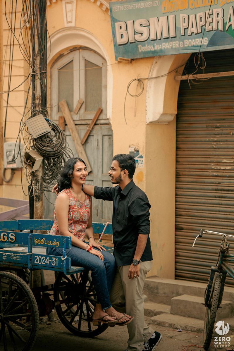 Candid photo of a couple sharing a romantic moment near a storefront with a cart in the streets of India.