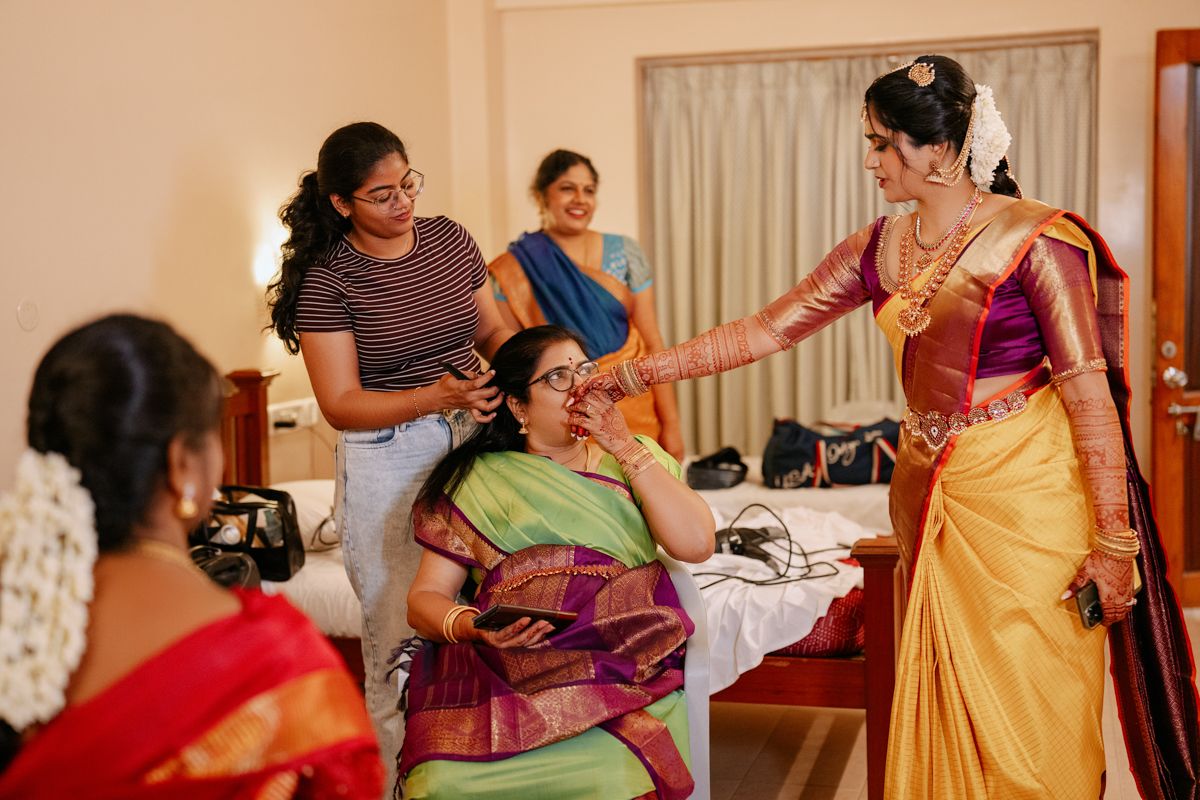 Wedding preparation scene in an indoor setting with women in traditional South Indian attire.