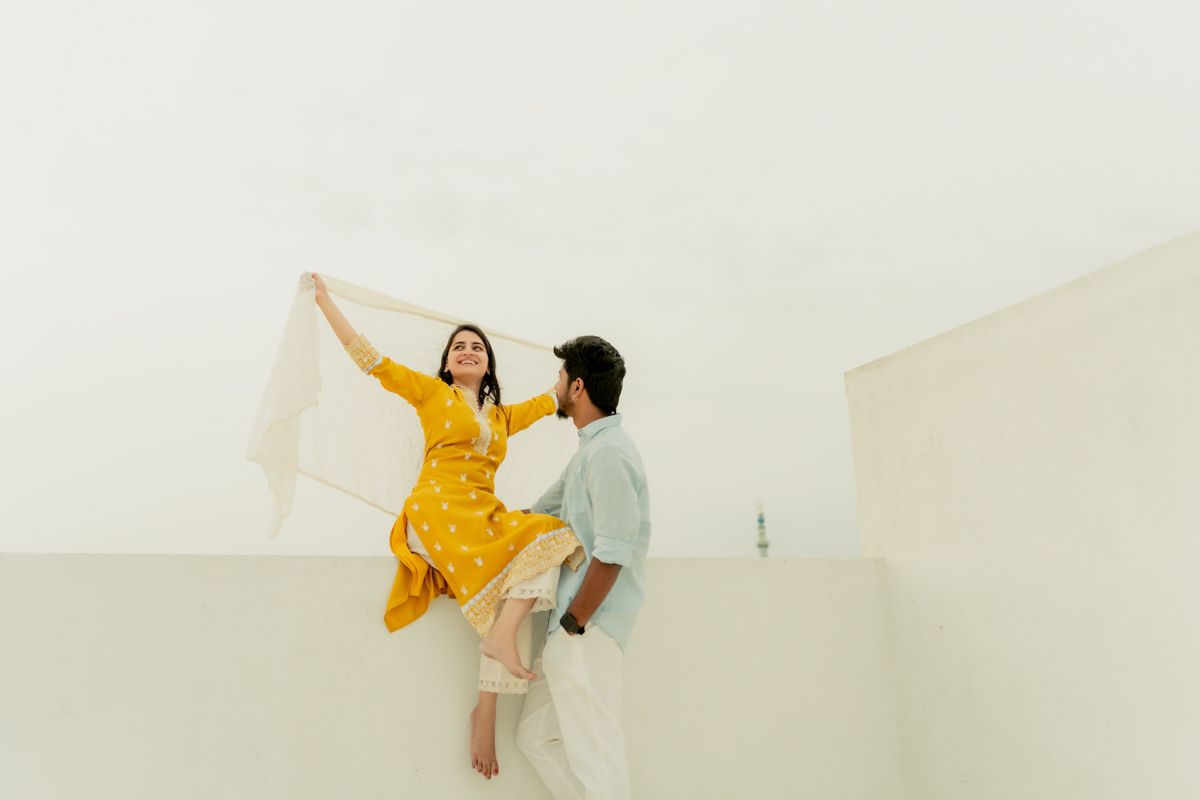 Carefree couple dancing together in a bright white room with one in a vibrant yellow dress.