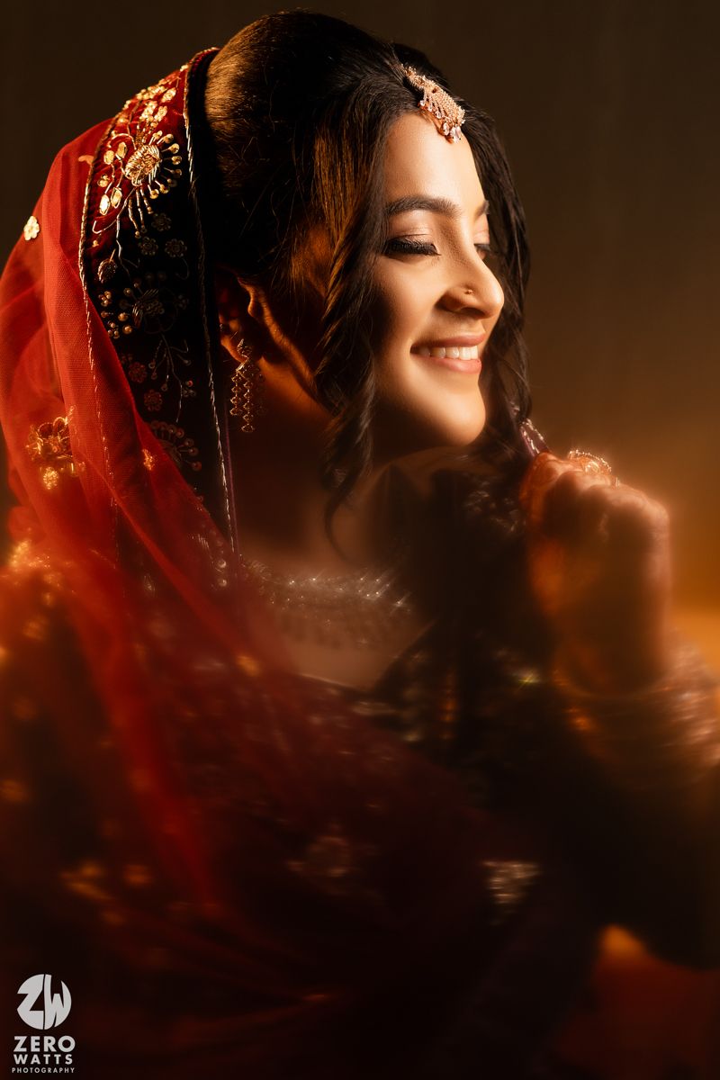Portrait of someone in traditional South Asian bridal attire with red dupatta and jewelry in warm lighting.