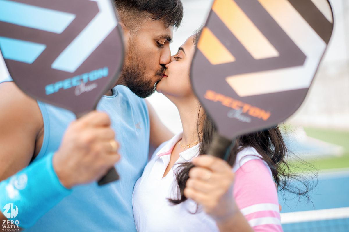 Intimate couple moment captured on a blue tennis court with sports equipment nearby.