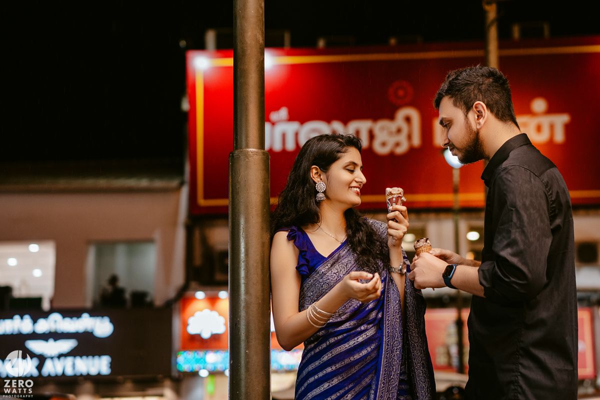 A couple shares a romantic moment under city lights with neon signs in the background.