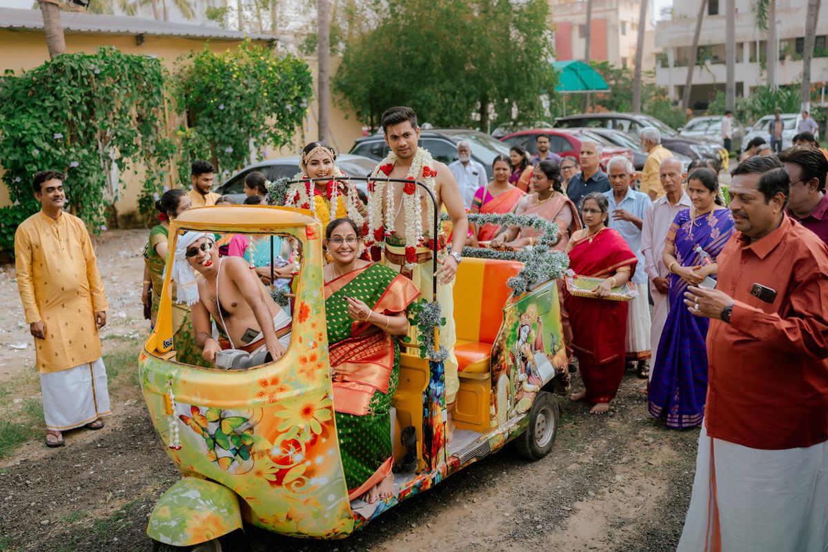 Festively decorated auto rickshaw with wedding guests in colorful traditional Indian attire gathering around.