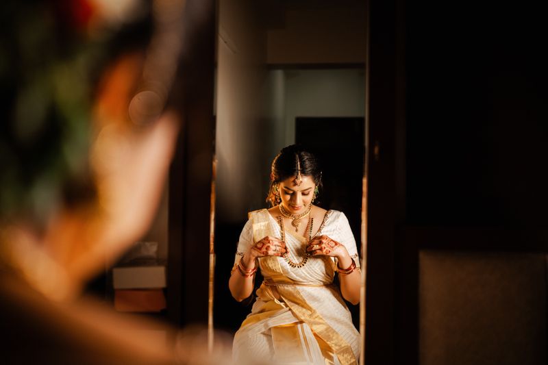 Warm candlelit reflection shows someone wearing traditional Indian attire looking into mirror during wedding preparations.
