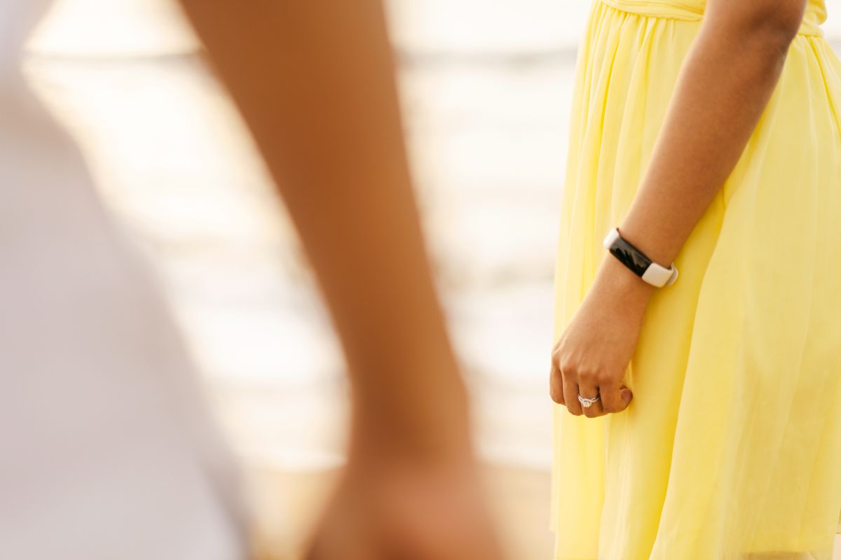 Partial view of a person wearing a flowing yellow dress and wristwatch with sunlit shadows casting on the fabric.