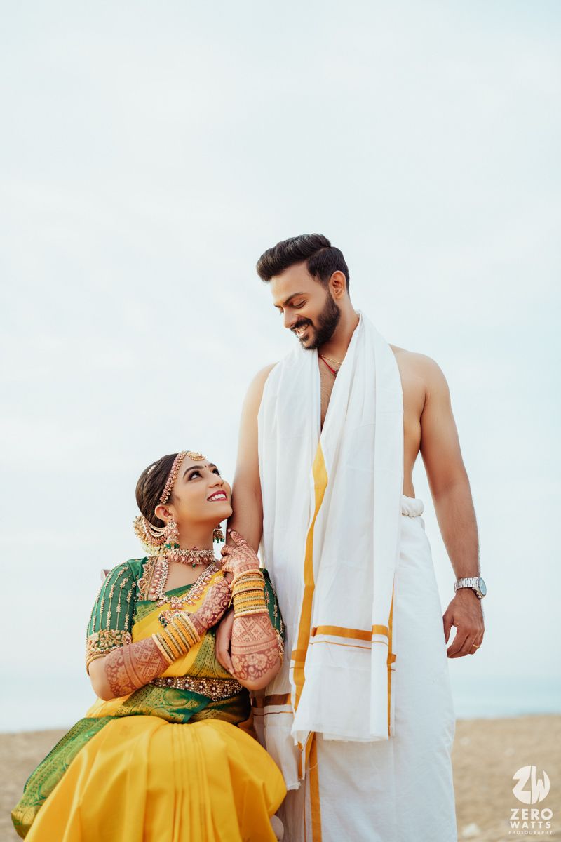 South Indian couple in traditional wedding attire posing against sky on beach.