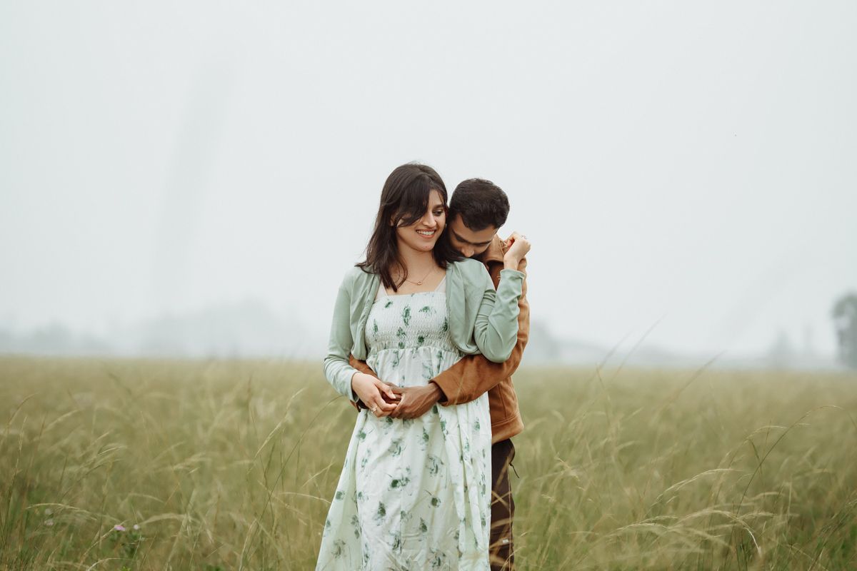 Romantic couple embracing in misty field wearing coordinated outfits.