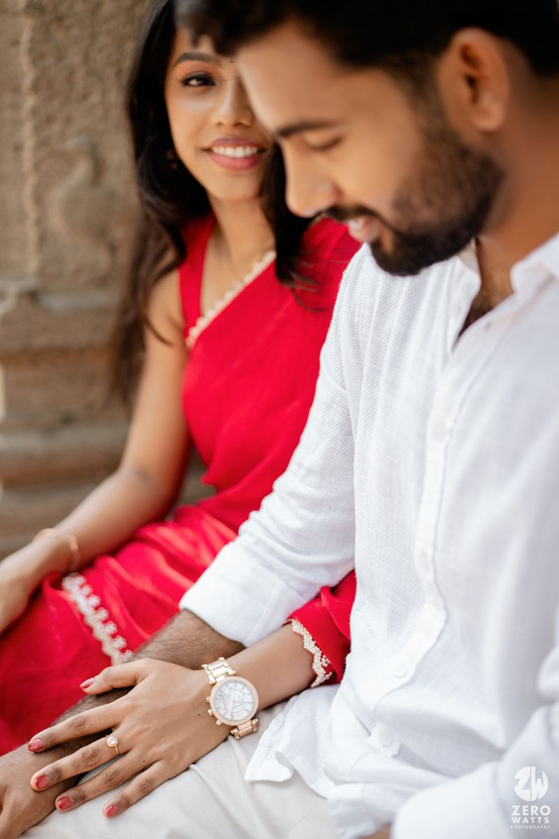 A couple shares an intimate moment in traditional Indian attire against a stone pillar backdrop.