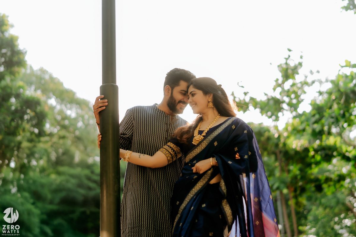A romantic couple in traditional Indian attire share an intimate moment while posing against a pole in a garden setting.