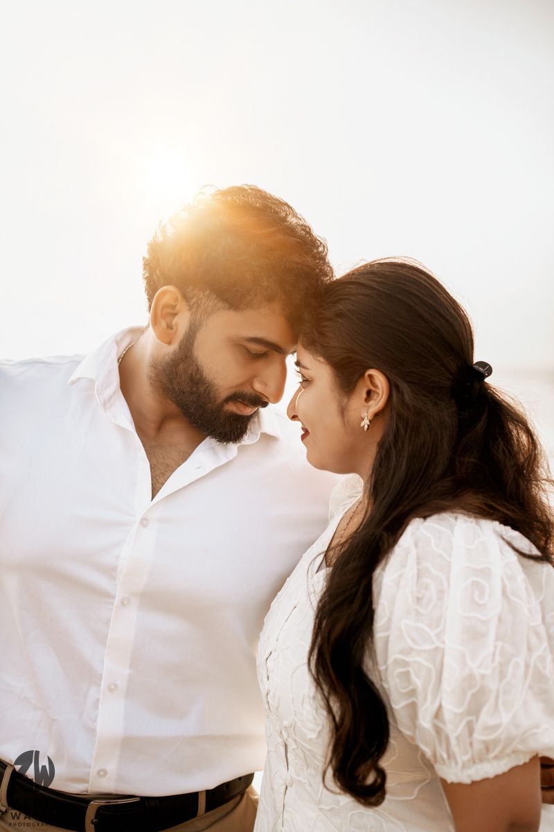 Romantic couple in white outfits share an intimate moment against bright sunlight in a minimalist setting.