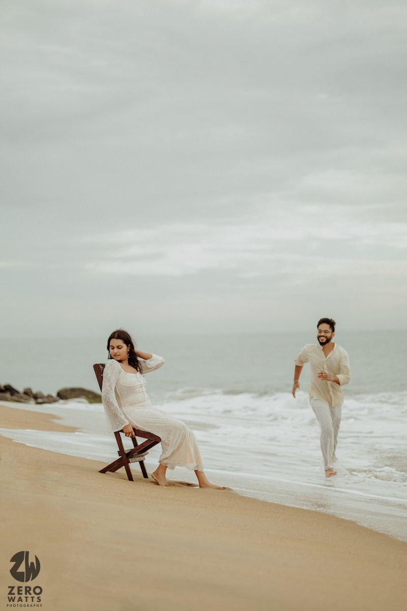 A playful beach photoshoot with a couple in white outfits against an overcast sky.