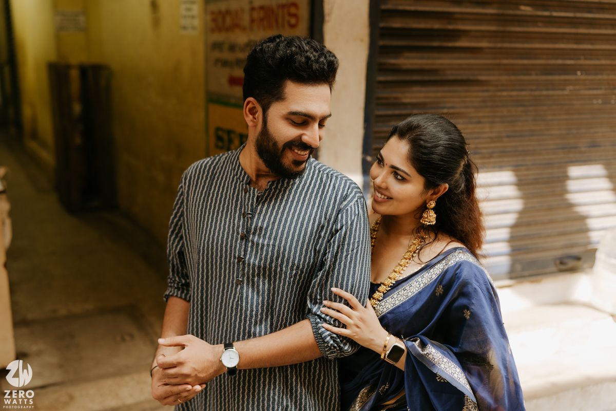 A couple in traditional South Asian attire share a tender moment on a sunlit street corner.