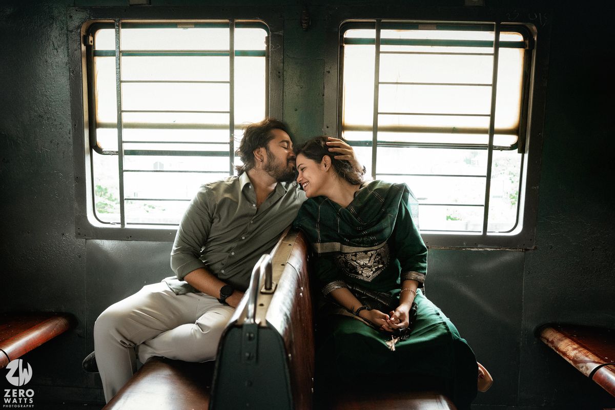 Two people share a tender moment on red seats inside a dimly lit vintage train car.