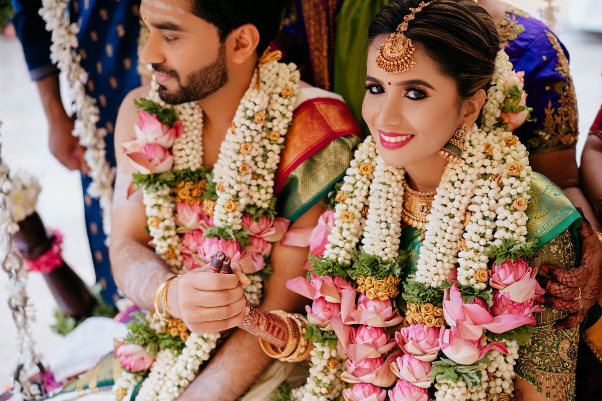 A couple in traditional South Indian wedding attire adorned with flower garlands and jewelry.
