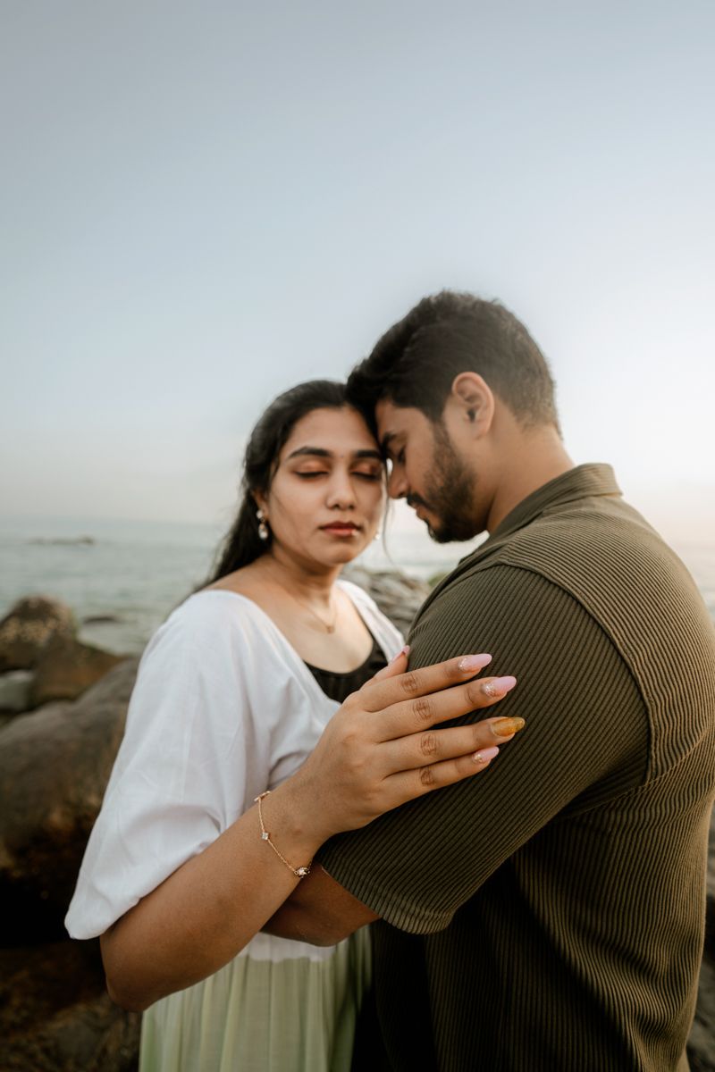 A romantic moment captured between a couple embracing on rocky coastal shores at sunset.