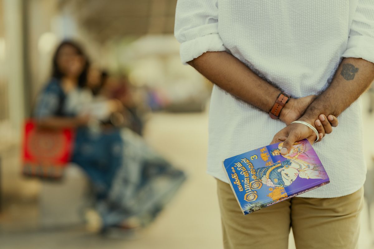 Person holding a credit card behind their back in a deceptive manner while standing in a public space.