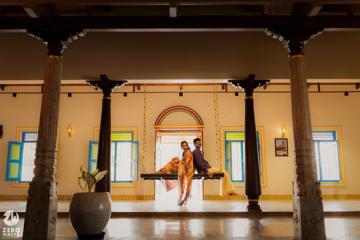 Couple dancing and posing in a grand vintage hall with ornate columns and arched windows.