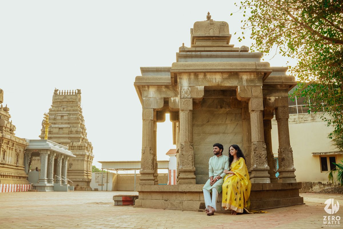 A couple poses at a traditional South Indian temple with ornate stone architecture and pillars.