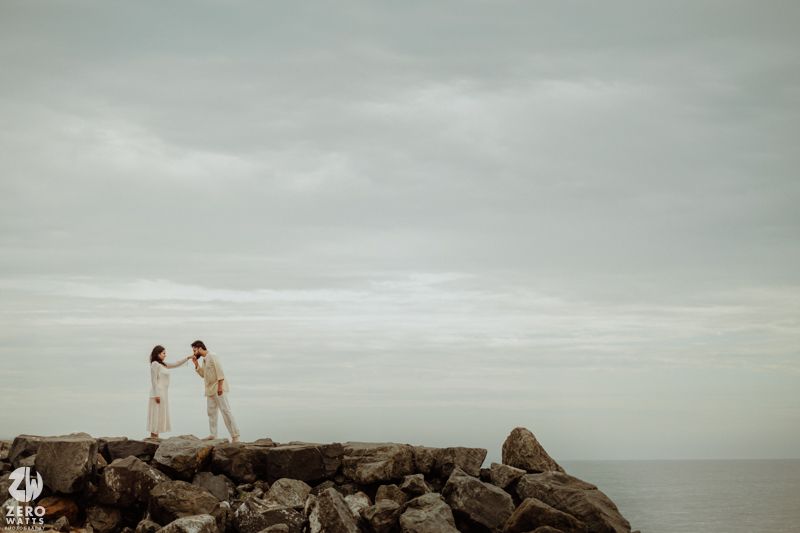 Couple standing on rocky coastal outcrop overlooking grey ocean.