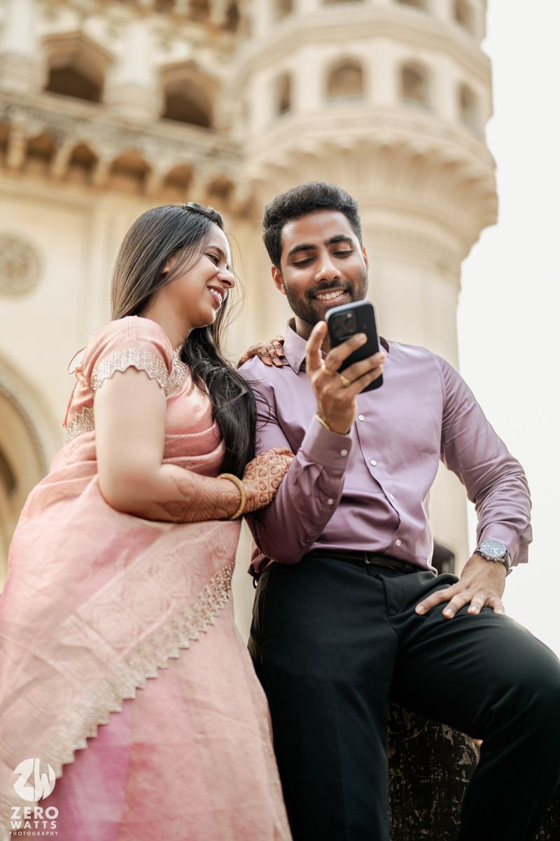 A couple sharing a laugh while looking at a phone near historic architecture.